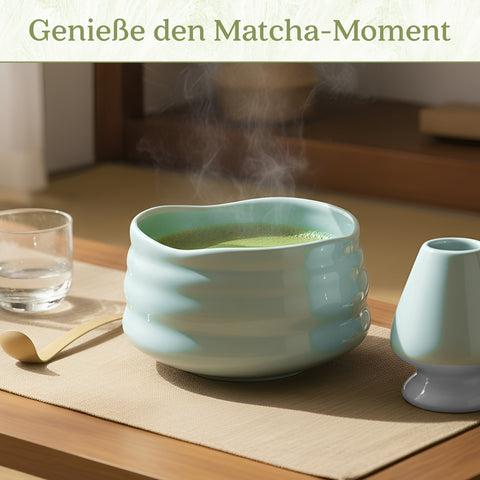 Gewurzladen Nafels Dampfender heißer Matcha Tee in einer hellblauen Schale neben einem Besenhalter und einem Löffel.