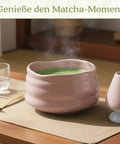 Gewurzladen Nafels Dampfender grüner Matcha-Tee in einer rosa Schale neben Besenhalter und Löffel.