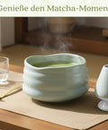 Gewurzladen Nafels Dampfender heißer Matcha Tee in einer hell minzgrünen Schale neben einem Besenhalter und einem Löffel.