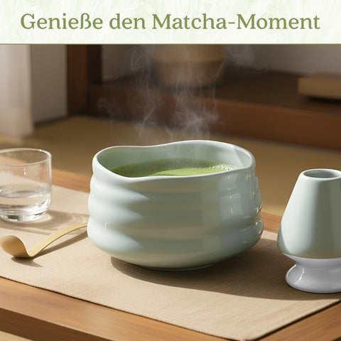 Gewurzladen Nafels Dampfender heißer Matcha Tee in einer hell minzgrünen Schale neben einem Besenhalter und einem Löffel.