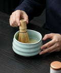 Gewurzladen Nafels Hände schlagen Matcha Tee in einer hellgrünen Keramikschale mit einem Bambusbesen auf.