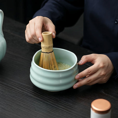 Gewurzladen Nafels Hände schlagen Matcha Tee in einer hellgrünen Keramikschale mit einem Bambusbesen auf.