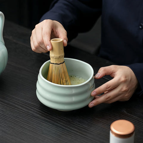 Gewurzladen Nafels Hände schlagen Matcha Tee in einer minzgrünen Keramikschale mit einem Bambusbesen auf.
