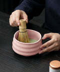 Gewurzladen Nafels Hände verquirlen grünen Matcha in einer rosa Keramikschale mit einem Bambusbesen.