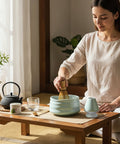Gewurzladen Nafels Frau bereitet Matcha Tee mit Besen und hell minzgrüner Schale auf einem Holztisch zu.