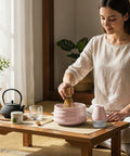 Gewurzladen Nafels Frau bereitet Matcha Tee mit Besen und rosa Schale auf einem Holztisch zu.