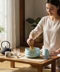 Gewurzladen Nafels Frau bereitet Matcha Tee mit Besen und hellblauer Schale auf einem niedrigen Holztisch zu.