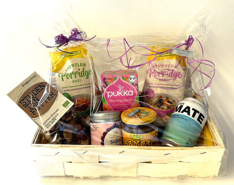 In Zellophan verpackter Korb mit Porridge, Tee, Nussmischung und verschiedenen Aufstrichen.