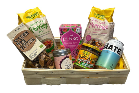 Geschenkkorb mit Bio-Frühstücksprodukten, darunter Porridge, Nüsse, Tee und Aufstriche.